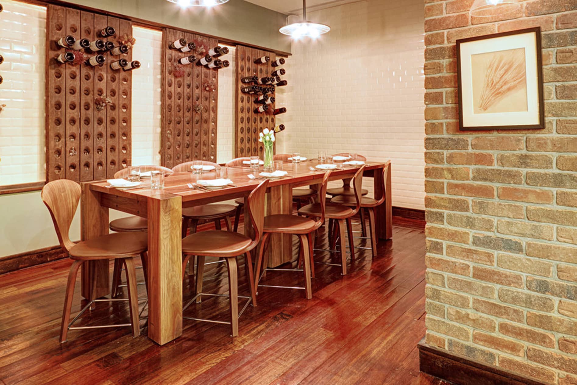 Custom Walnut Dining Table and Chairs at Bread & Tulips Restaurant by SENTIENT Interior of Bread & Tulips restaurant showcasing a custom walnut communal dining table and sculptural wood chairs by SENTIENT, with wine bottle wall displays and a warm, rustic ambiance.