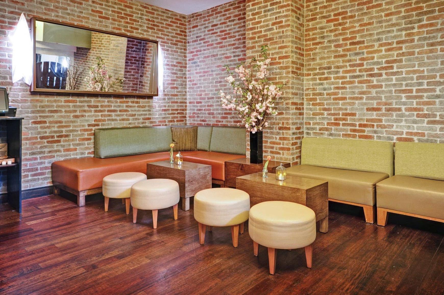 Custom Lounge Furniture for Bread & Tulips Restaurant by SENTIENT Cozy lounge seating area at Bread & Tulips restaurant featuring custom upholstered banquettes, leather ottomans, and minimalist wood block tables by SENTIENT, set against rustic exposed brick walls.