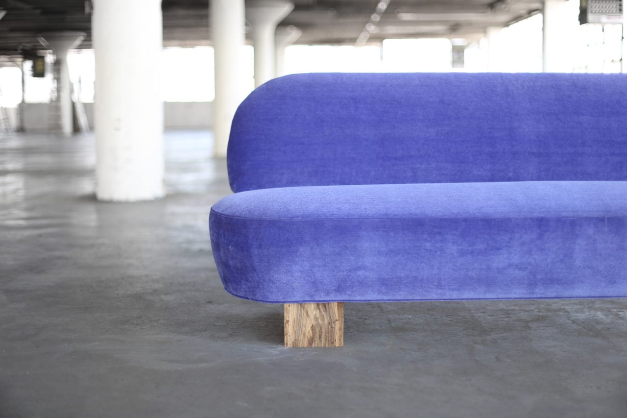 a half detail view of a SENTIENT contemporary designed custom sofa in luxury blue velvet with wood beam leg