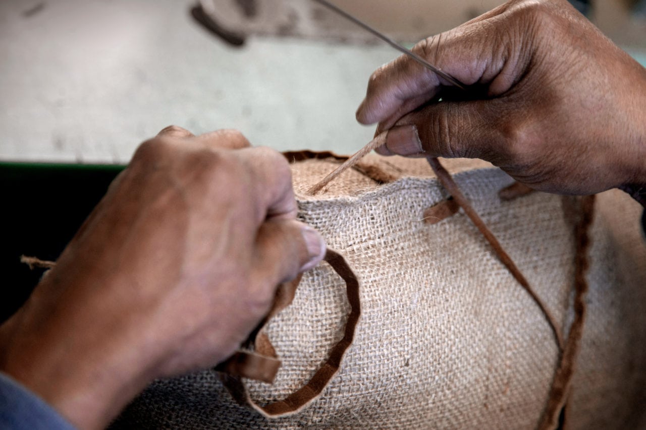 Handmade upholstery for our custom furniture modelsTwo hands stitching custom natural luxury fabric in SENTIENT workshop