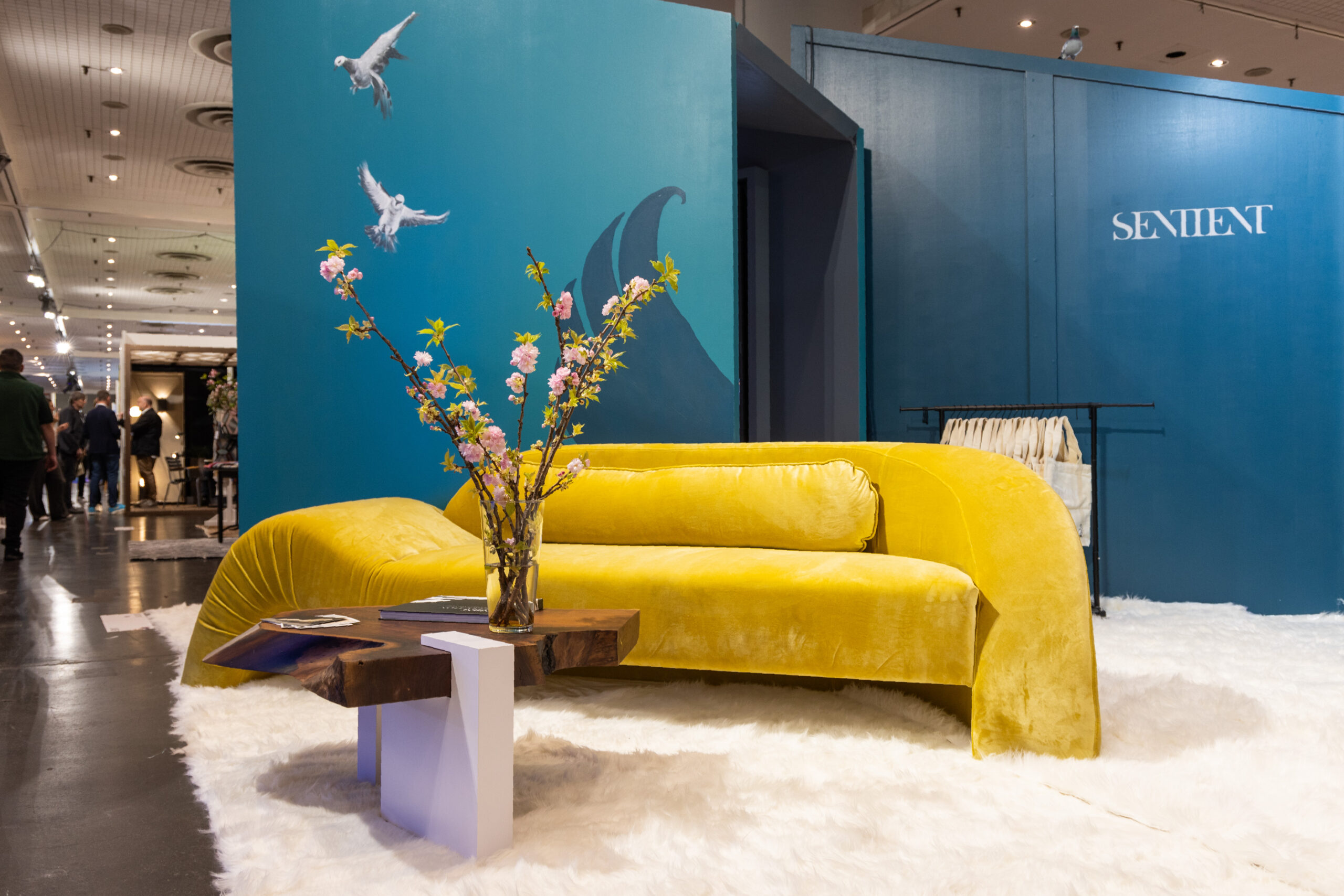 Sentient Aeon Sofa at ICFF 2024 The Sentient Aeon Sofa on display at ICFF 2024, showcasing its curved silhouette and vibrant yellow velvet fabric, set in a stylish booth environment.