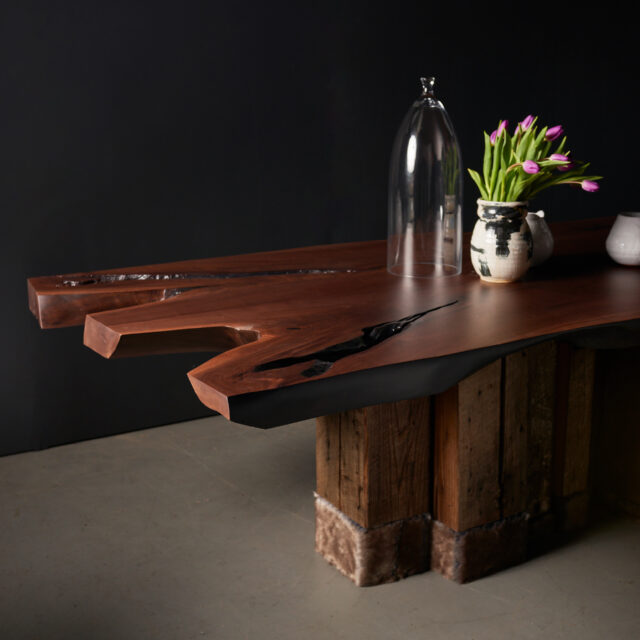 The SENTIENT Evolution Table featuring a live edge walnut top with dramatic grain and unique void details. The rustic reclaimed wood base adds character and contrasts beautifully with the organic tabletop design.