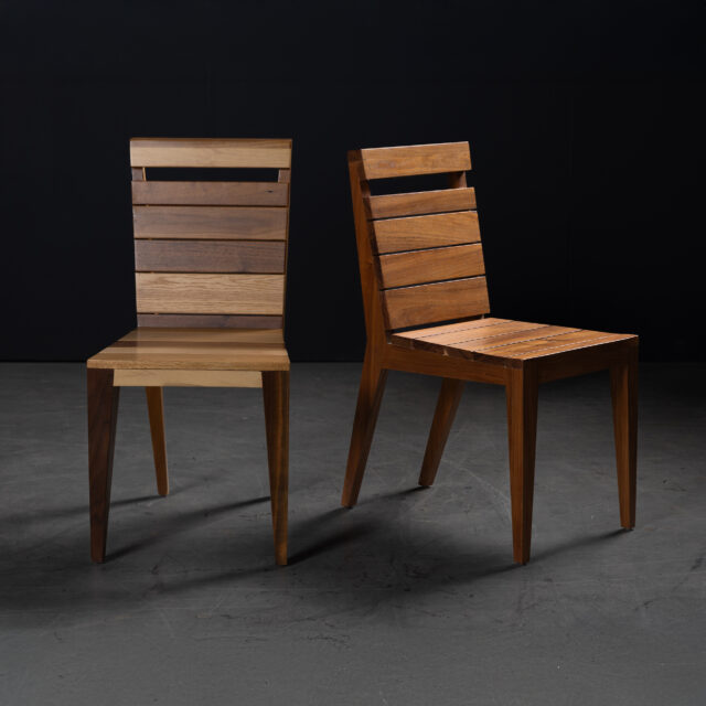 A pair of SENTIENT Angle Chairs showcasing sleek designs, one crafted from mixed hardwoods and the other from rich walnut. The chairs feature slatted backs and minimalist aesthetics, perfect for modern interiors.