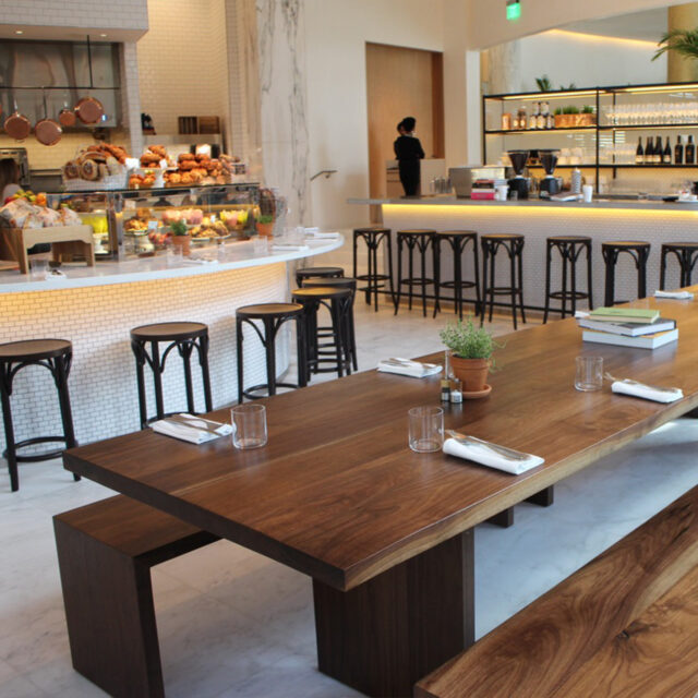 A contemporary cafe interior featuring SENTIENT custom communal dining tables crafted from solid walnut with clean lines. The tables create a warm and inviting atmosphere, perfect for group dining and gatherings.