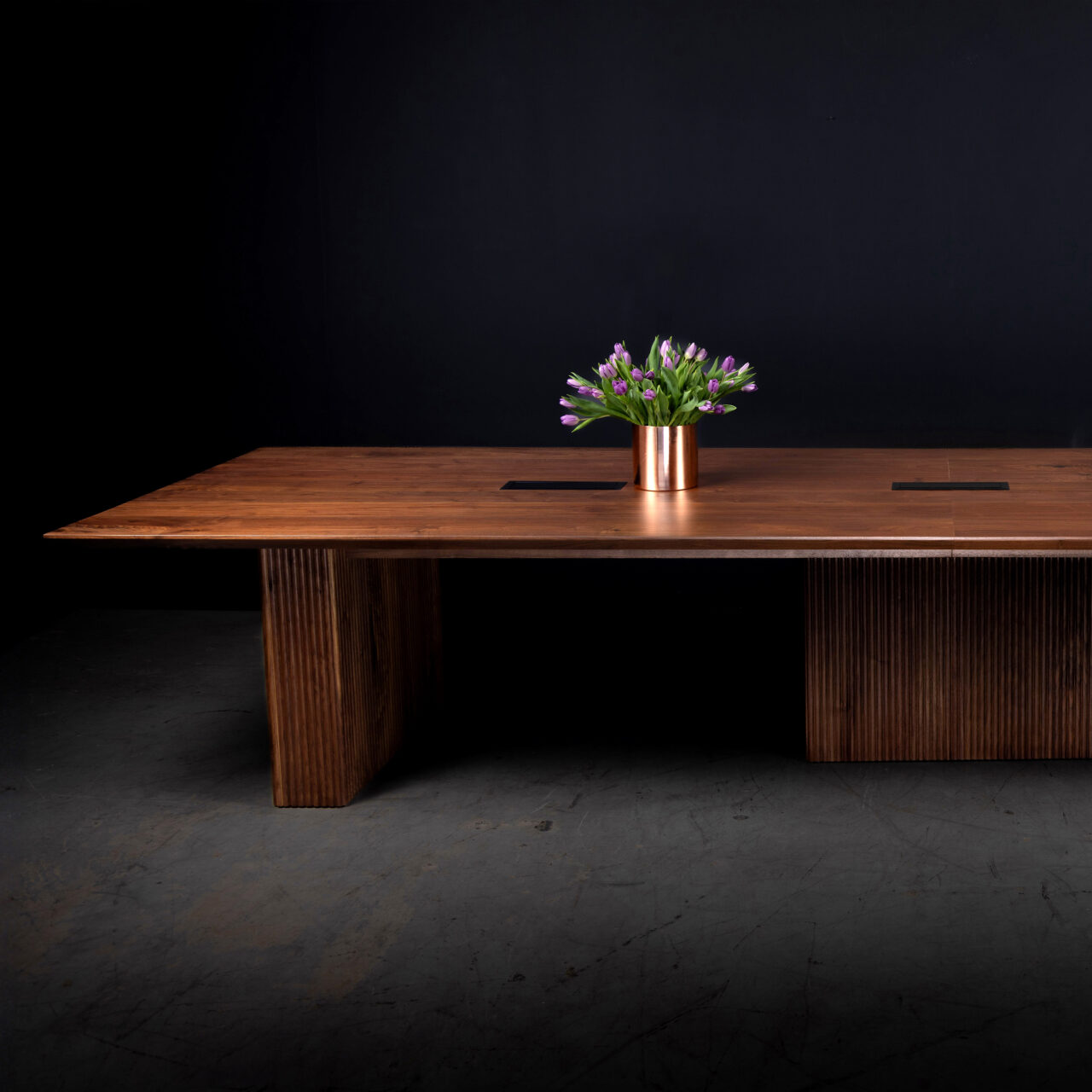 A SENTIENT custom conference table crafted from walnut wood, featuring a spacious top and a fluted base. The design includes integrated functionality and a modern aesthetic, perfect for sophisticated office spaces.
