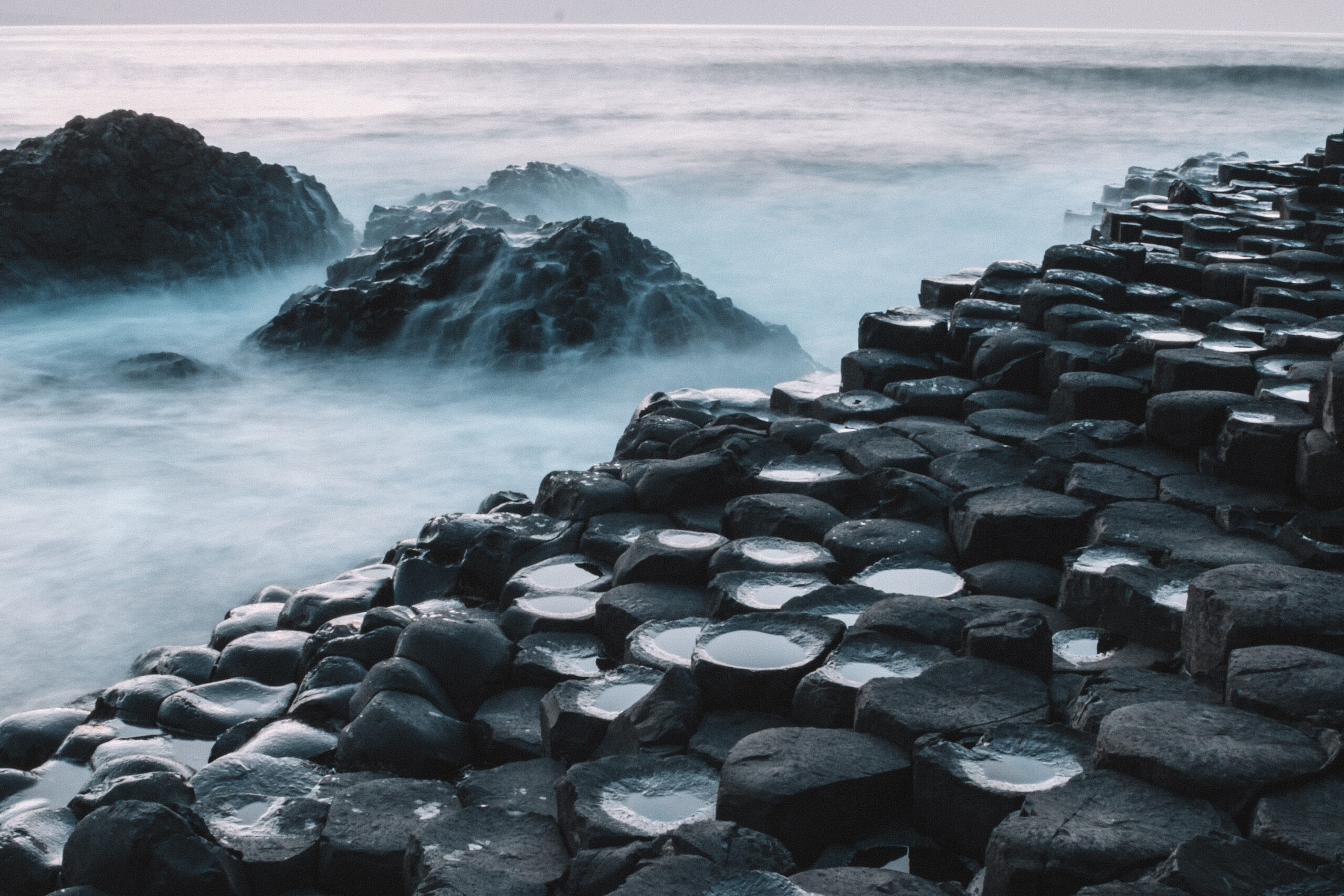 Giant’s Causeway Rocks in Ireland Natural hexagonal rock formations at Giant’s Causeway, Ireland, with the ocean waves washing over them, capturing the rugged beauty of this iconic geological site.
