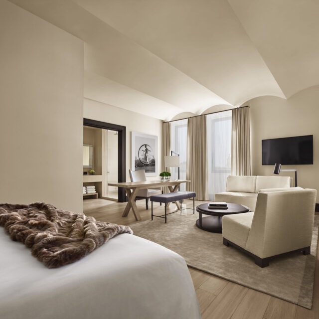 A luxury hotel room featuring SENTIENT custom furniture, including a modern wooden desk, upholstered seating, and a round coffee table. The design blends neutral tones, natural materials, and sophisticated aesthetics for a serene ambiance.