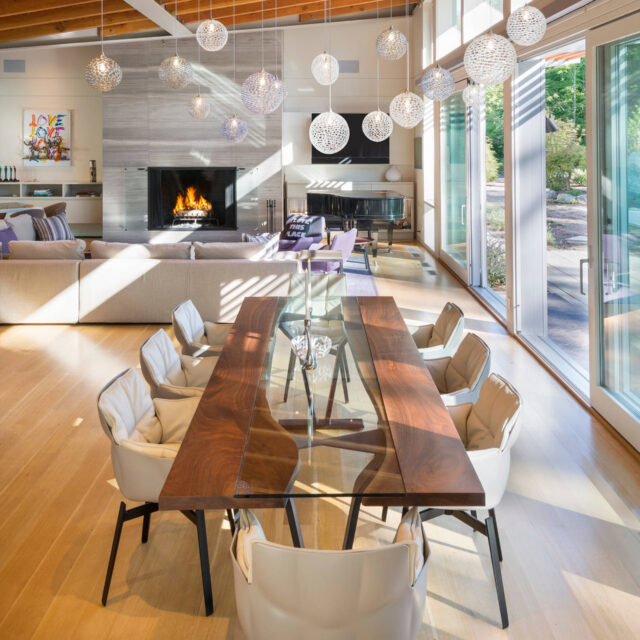 A luxury residential dining area featuring a SENTIENT custom live edge walnut dining table with a glass inlay. The space is adorned with modern lighting, plush seating, and a fireplace for a warm and inviting ambiance.