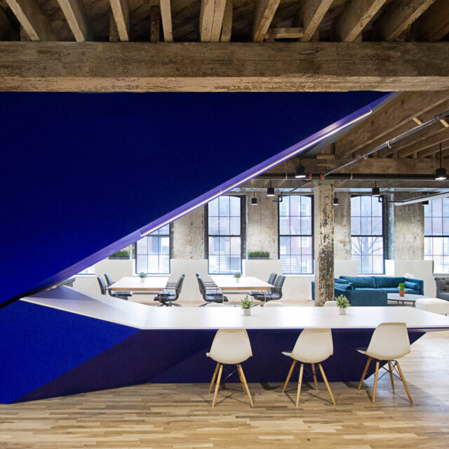 A modern office interior featuring SENTIENT custom furniture, including a bold geometric table and stylish seating. The space combines contemporary design elements with an industrial aesthetic for a functional and vibrant workplace.