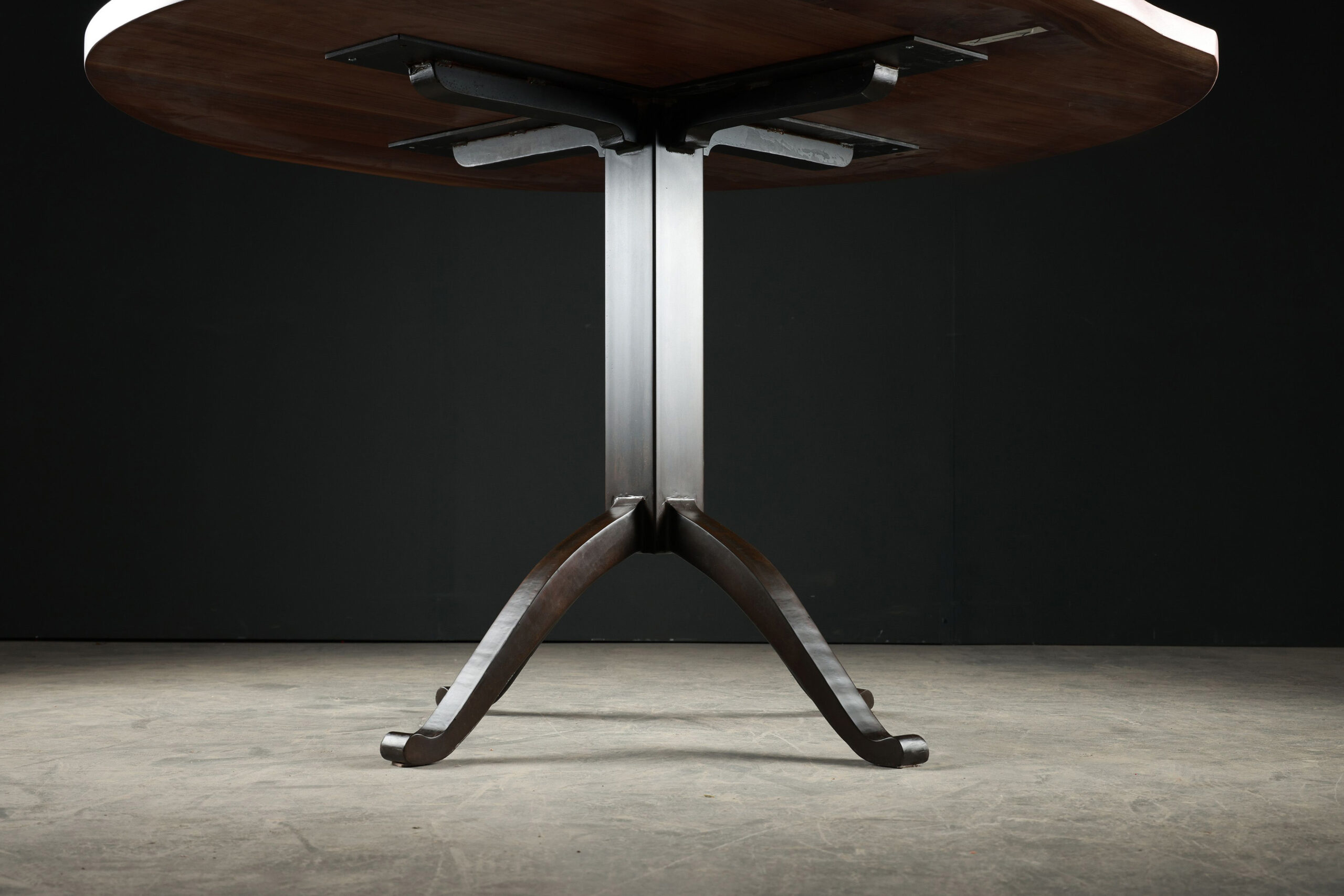 Close-up view of the custom pedestal table base by SENTIENT, showcasing its sturdy, artistic design in dark metal.