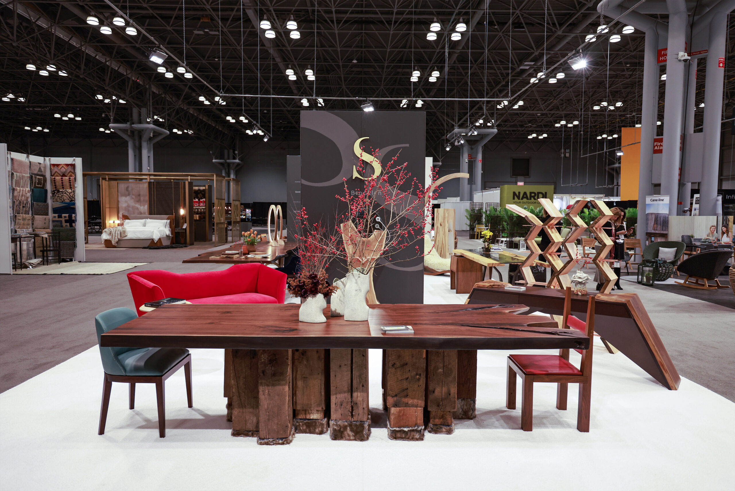 SENTIENT Furniture Booth at ICFF NYC Featuring Evolution Table The SENTIENT Furniture booth at ICFF NYC showcasing the Evolution live edge table, decorated with vibrant red berries and surrounded by contemporary seating, highlighting modern and artistic furniture designs.