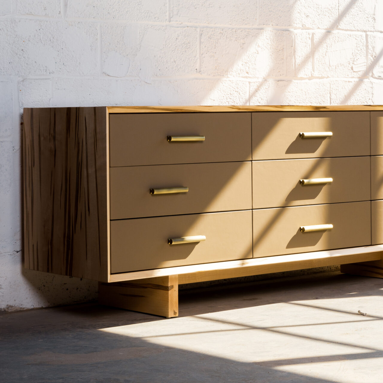 A modern dresser by SENTIENT featuring leather-front drawers, brass handles, and a spalted maple body. The elegant design combines luxury materials with minimalist functionality, perfect for sophisticated interiors.