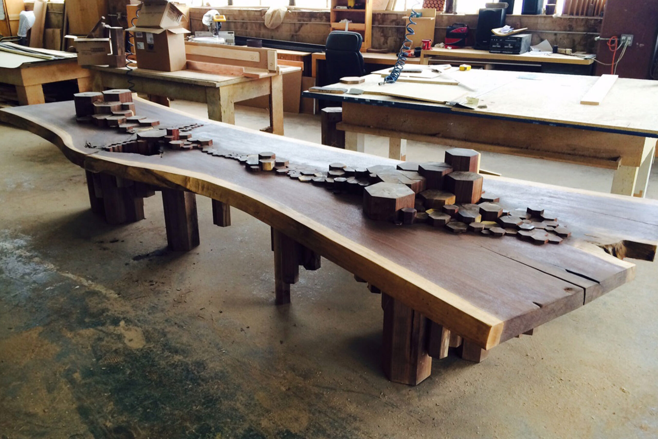 Causeway Table Making Of at SENTIENT Workshop The process of creating the Causeway Table at the SENTIENT workshop, featuring raw hexagonal pieces and wood blocks being arranged on the tabletop.