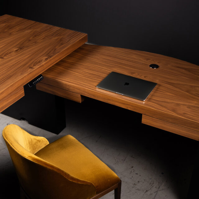 A sleek custom walnut desk with adjustable height, paired with a luxurious yellow velvet chair, showcasing modern workspace design.