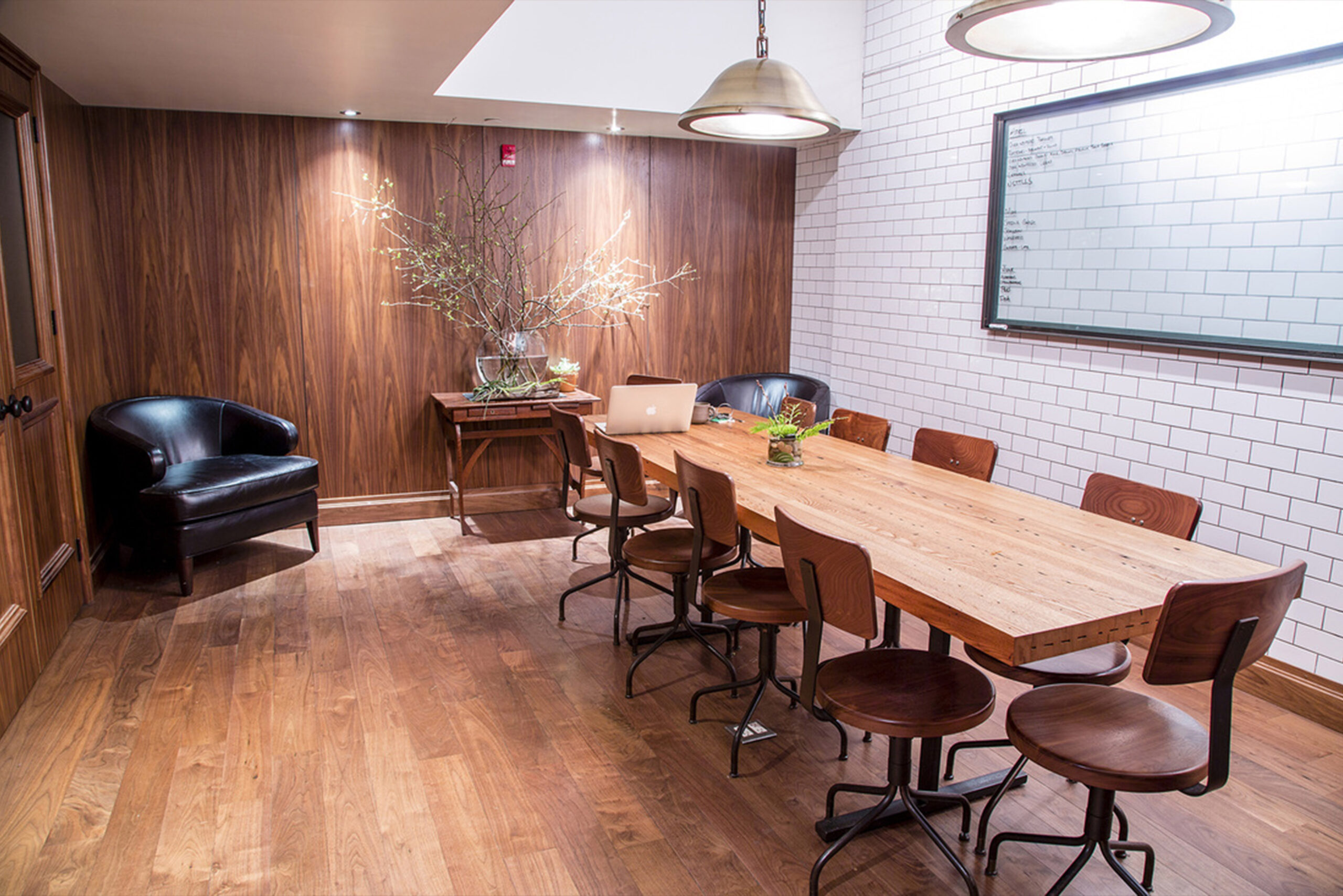Custom Conference Table for Atera Restaurant by SENTIENT Warm-toned wood conference room featuring a custom rectangular table by SENTIENT with a natural grain top, vintage-inspired swivel chairs, leather lounge seating, and a white tiled wall in Atera Restaurant, New York.