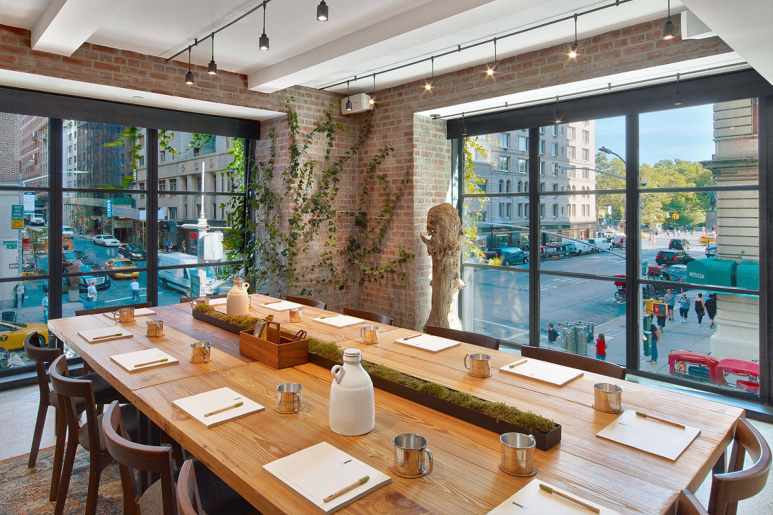 Custom Wood Table by SENTIENT – Jams Restaurant with Central Park View Custom-made wooden dining table by SENTIENT at Jams restaurant in New York City, featuring a minimalist tabletop arrangement, greenery centerpiece, and expansive corner windows with views of Central Park and Manhattan streets.<br />