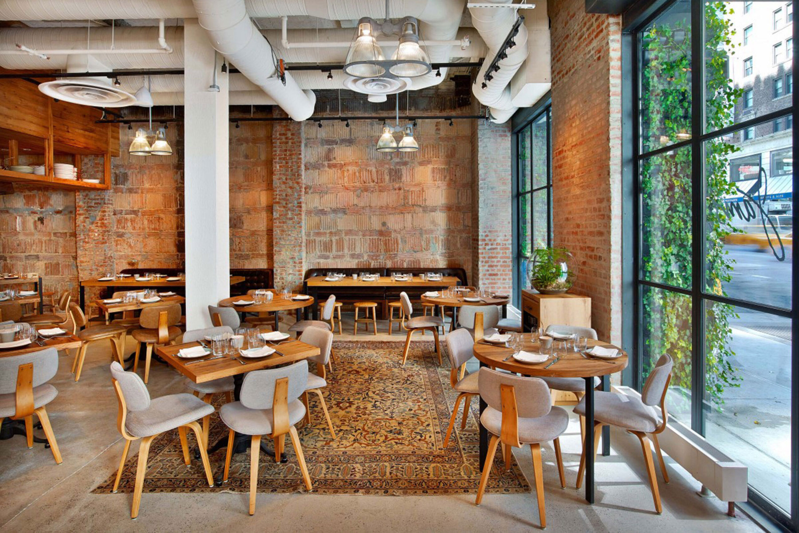 Custom Dining Tables and Chairs by SENTIENT at Jams Restaurant, NYC Interior of Jams restaurant in NYC featuring custom-made wood dining tables and chairs by SENTIENT, with exposed brick walls, large industrial windows, and natural daylight highlighting the modern rustic aesthetic.