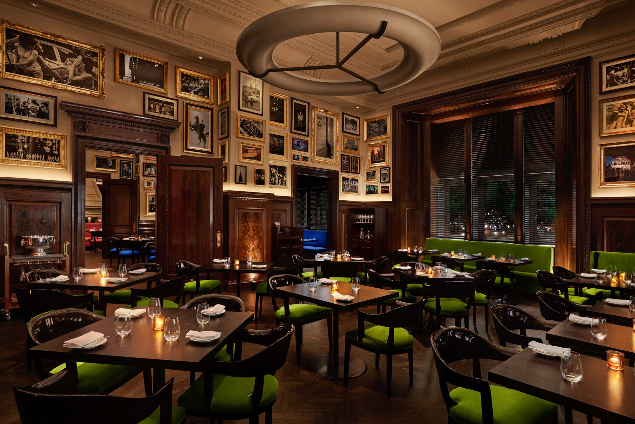 The Clocktower Green Room Restaurant with Custom SENTIENT Tables Interior of The Clocktower Green Room in New York City, featuring custom-made dark wood dining tables by SENTIENT, paired with black chairs upholstered in vibrant green fabric, surrounded by classic wood paneling and framed photography.<br />