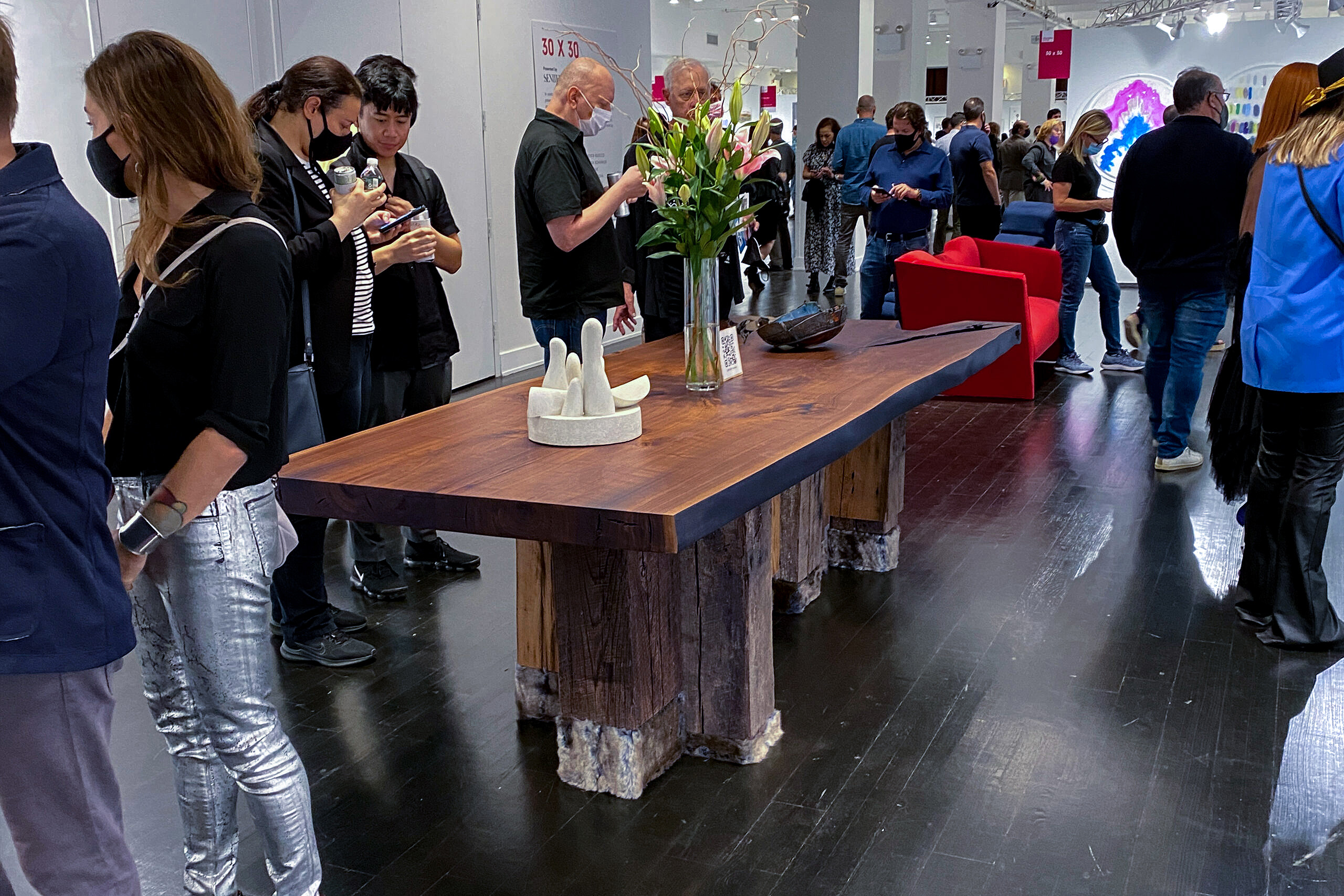 SENTIENT Evolution Live Edge Table at AAF Art Show Visitors admiring the SENTIENT Evolution live edge table at the Affordable Art Fair (AAF), with floral decorations enhancing the rustic and artistic wood design on display.